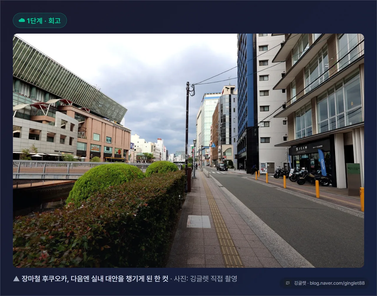 후쿠오카 여행 실사진 - 비 오는 거리나 우산 쓴 풍경(인물 얼굴은 블러). 캡션 “장마철 후쿠오카, 다음엔 실내 대안을 챙기게 된 한 컷”. GPS·위치정보 제거
